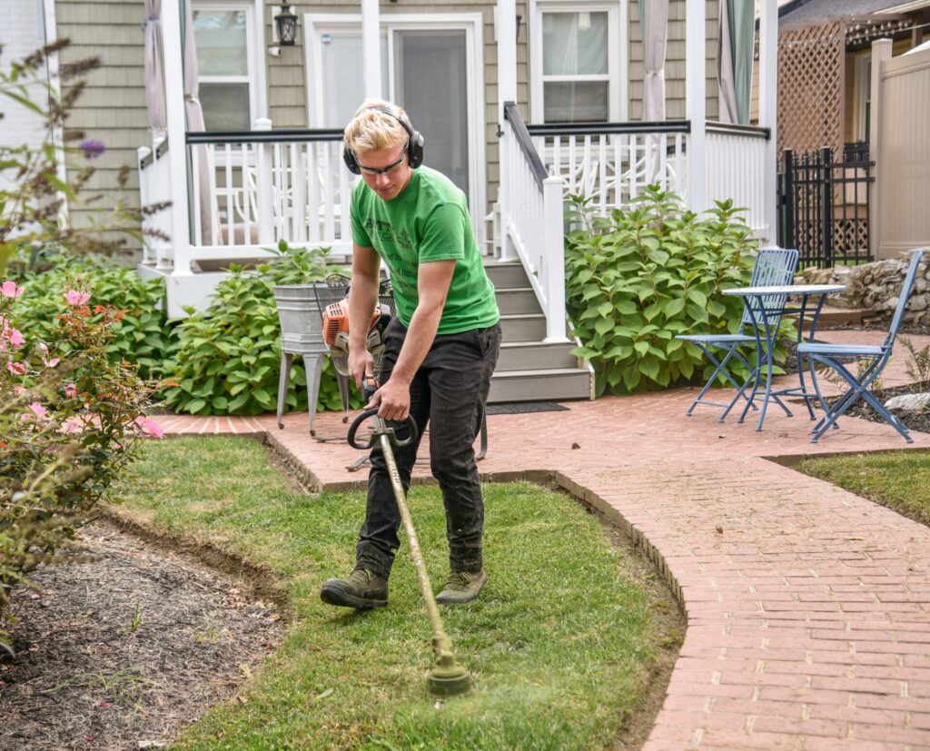 muž se chrániči sluchu seká trávník před rodinným domem